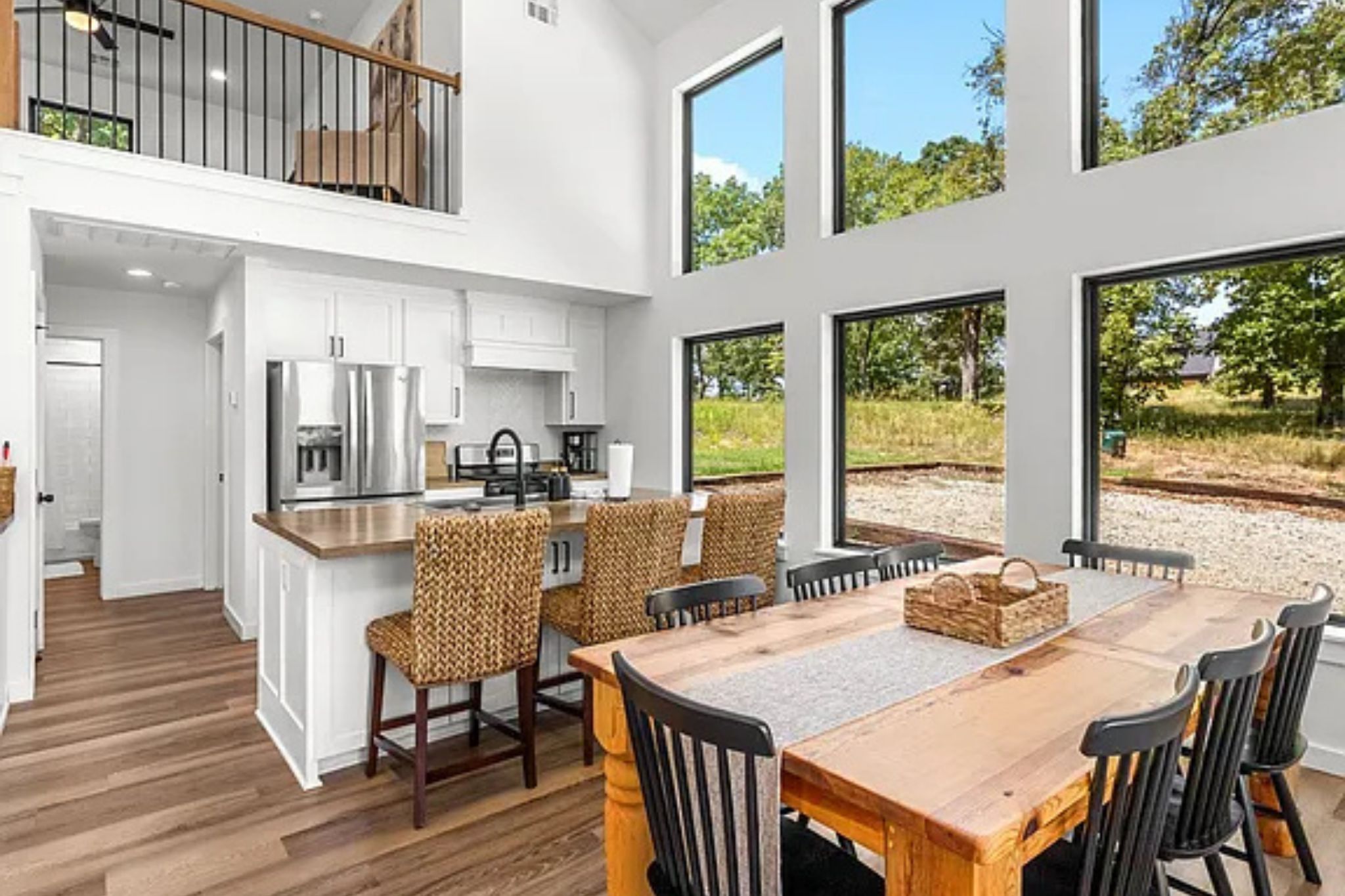 Une cuisine spacieuse avec des meubles blancs, une table à manger en bois et une vue sur l’extérieur grâce à de grandes fenêtres.