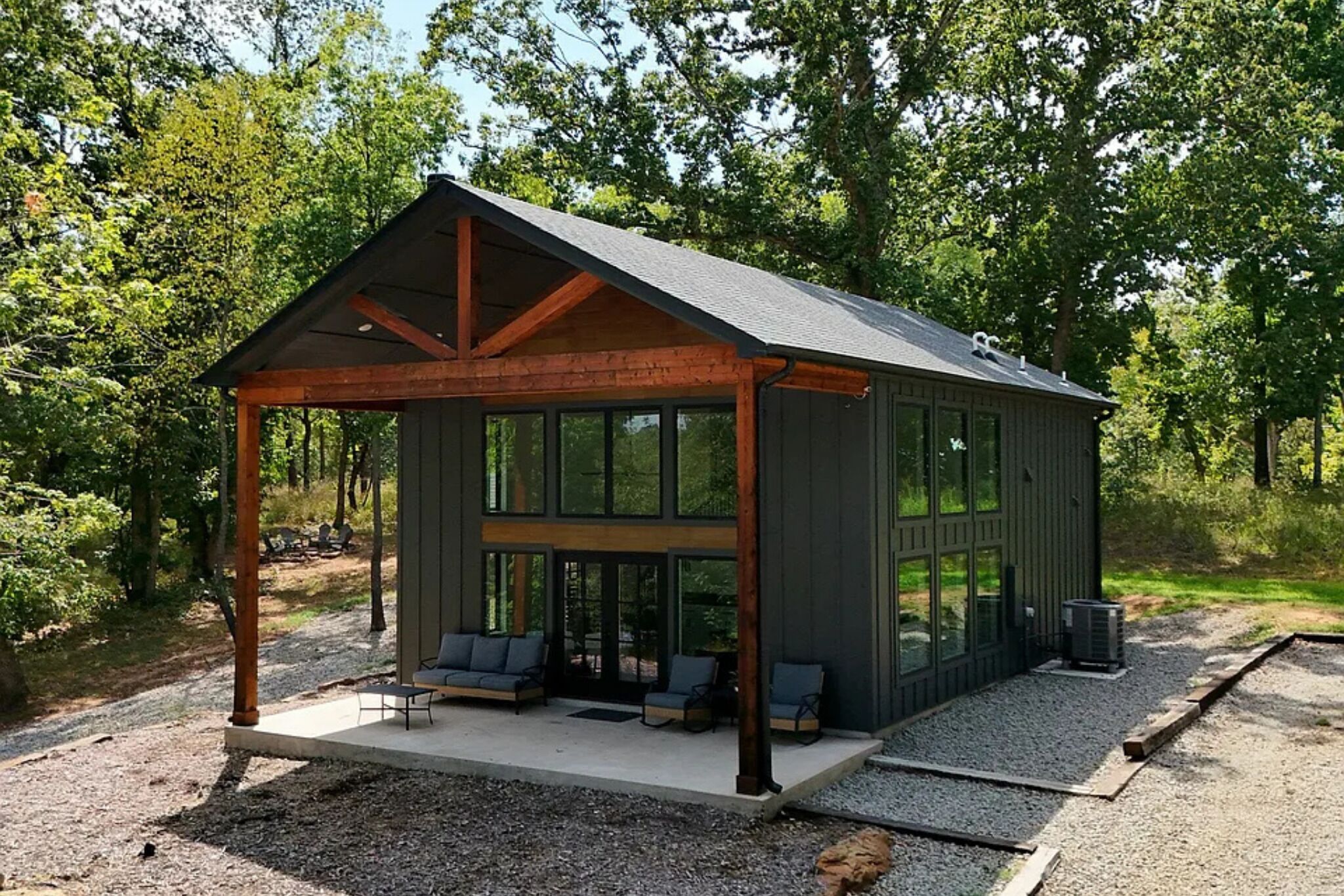 Une cabane dotée d’un porche abrité, de grandes fenêtres et d’un espace salon extérieur.