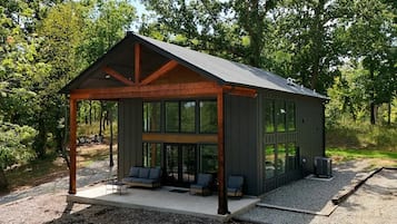 Une cabane dotée d’un porche abrité, de grandes fenêtres et d’un espace salon extérieur.