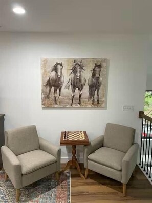 Een kamer met twee fauteuils, een houten tafel met een schaakbord en een schilderij van paarden aan de muur.