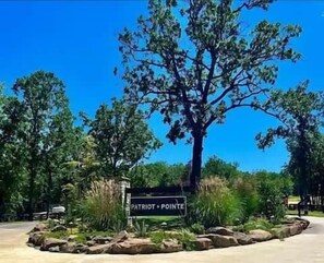 Un panneau indiquant « Patriot Pointe », avec un grand arbre au premier plan et un ciel bleu dégagé en arrière-plan.