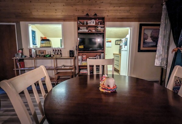 Un coin repas comprenant une table en bois, des chaises, un téléviseur et une bibliothèque.