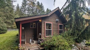 A small wooden cabin with a porch, surrounded by dense forest. - Whimsical and cozy cottage on a homestead in the North Cascades (Concrete)