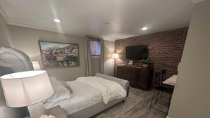 Ein Schlafzimmer mit Bett, Schminktisch, Fernseher an einer Ziegelwand und einem Fenster mit Vorhängen.