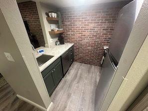 A compact kitchen with a brick backsplash, a built-in dishwasher, and a stainless steel refrigerator.