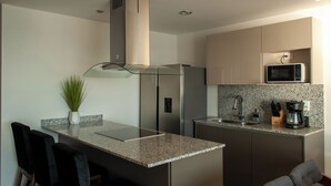 Una cocina moderna con encimera de granito, electrodomésticos de acero inoxidable y una pequeña isla con taburetes de bar.