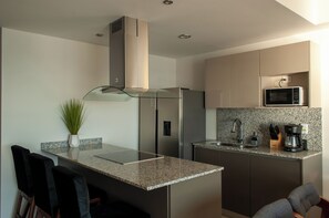 A modern kitchen with a granite countertop, stainless steel appliances, and a small island with bar stools. - Malecon Love (Mazatlán)