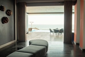 A modern room with a large window overlooking a pool and the sea. There are two sofas and a dining table with chairs. - Malecon Love (Mazatlán)
