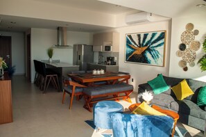 A modern living room with a dining area, a grey sofa with colorful cushions, and a large abstract painting on the wall. - Malecon Love (Mazatlán)