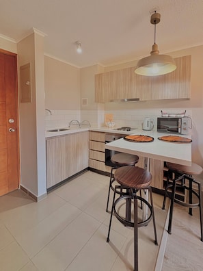 A modern kitchen with a white countertop, wooden cabinets, a microwave, and two bar stools. - Lodge with a View of the Volcano | Wi-Fi + Heating (Pucon)