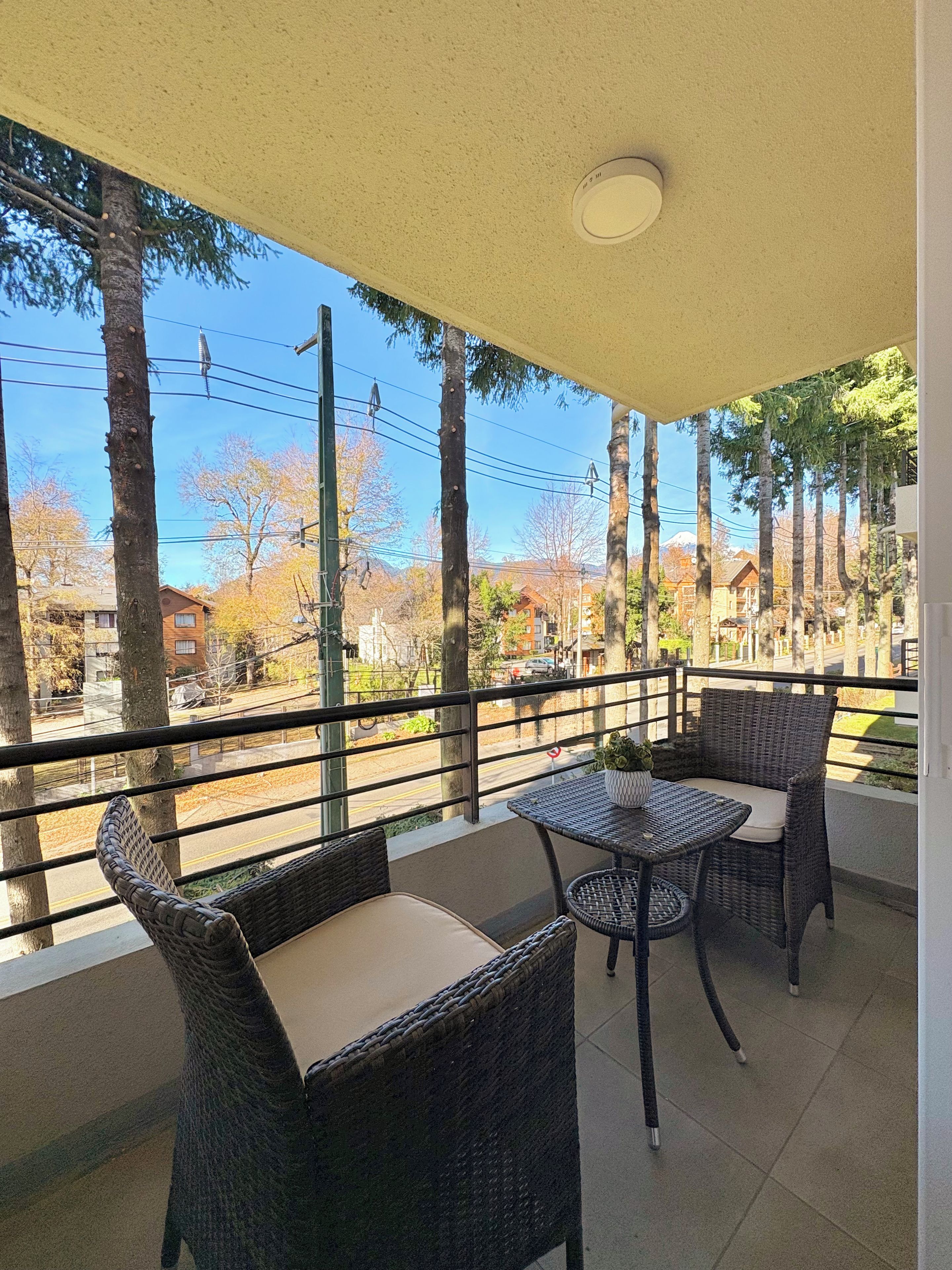 Un balcon avec des meubles en osier, une vue sur une rue et une montagne à l’horizon.