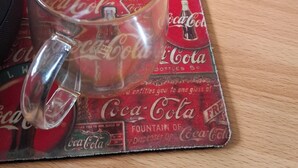 A glass mug on a Coca-Cola themed coaster, a keyboard, and a desk with various items including a spray bottle and a small container. - New and cozy apartment in exclusive area (Pucon)