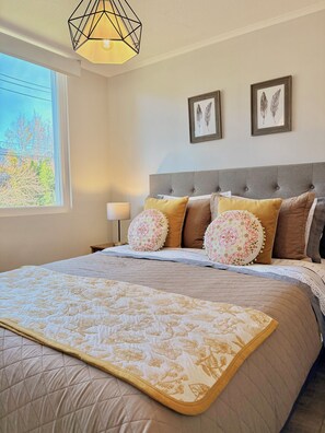 A bedroom with a large bed, a nightstand, a lamp, and two framed pictures on the wall. - Lodge with a View of the Volcano | Wi-Fi + Heating (Pucon)