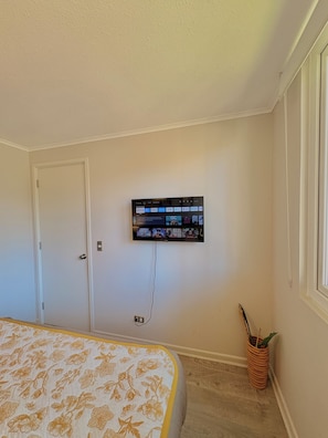 A bedroom with a bed, a mounted TV, a door, and a potted plant. - Lodge with a View of the Volcano | Wi-Fi + Heating (Pucon)