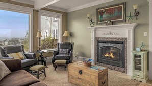 A living room with a fireplace, leather chairs, a wooden chest, and a view of the city. - Castello Del Mare - Ocean views, Hot tub, Dogs OK (Newport)