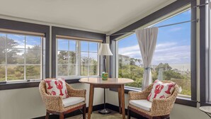A corner room with two wicker chairs, a small table, and large windows offering a view of greenery and buildings. - Castello Del Mare - Ocean views, Hot tub, Dogs OK (Newport)