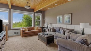 A spacious living room with a wooden ceiling, large windows, a brown leather sofa, a striped couch, and a dark wooden coffee table. - Castello Del Mare - Ocean views, Hot tub, Dogs OK (Newport)