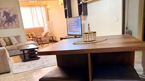 Un salon moderne avec une table à manger en bois, des bancs rembourrés, un téléviseur à écran plat et un objet décoratif posé sur la table.