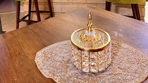 Une cuisine moderne avec un comptoir en marbre, deux tabourets de bar verts, une table à manger en bois agrémentée d’un élément décoratif central et des luminaires suspendus.