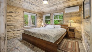 A wooden cabin bedroom with a bed, nightstands, a lamp, and large windows.