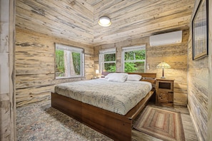 Une chambre dans une cabane en bois, avec un lit, des tables de chevet, une lampe et de grandes fenêtres.