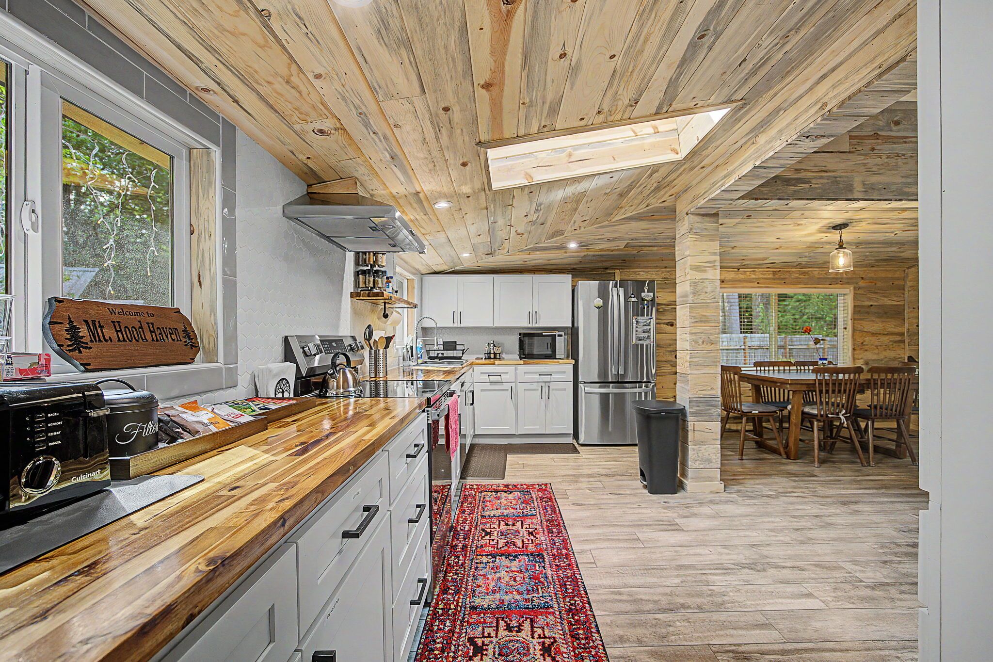 Eine moderne Küche mit Holzbalkendecke, weißen Schränken und einem roten Teppich mit Muster.