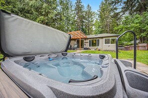 Un bain à remous avec une terrasse en bois, un patio couvert et une maison en arrière-plan.