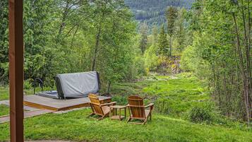 A deck with outdoor furniture, a covered grill, and a view of a forested valley.