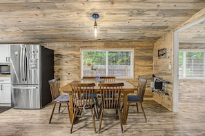 Un intérieur en bois comprenant une table à manger, des chaises, un réfrigérateur et une fenêtre avec des stores.
