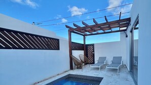 Area piscina moderna all'aperto con una pergola, lettini e cielo azzurro.