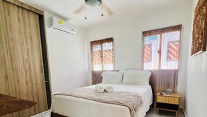 Una camera da letto con un letto, una ventola a soffitto, un comodino e una finestra con tende.