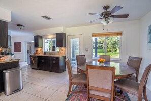 A modern kitchen with dark cabinets, a stainless steel refrigerator, and a dining area with a round table and chairs. - Spacious 7-bedroom house in delightful Southwest Ranches with AC (Southwest Ranches)