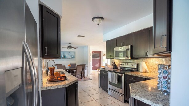 A modern kitchen with dark cabinets, stainless steel appliances, and a granite countertop. - Spacious 7-bedroom house in delightful Southwest Ranches with AC (Southwest Ranches)