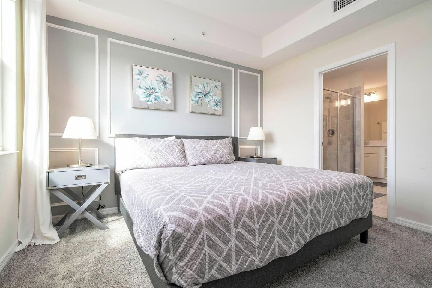 A bedroom with a large bed, two bedside tables with lamps, a nightstand, and a door leading to a bathroom.