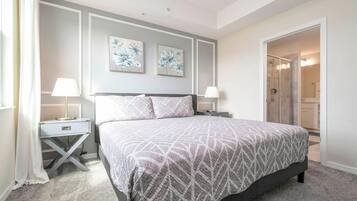 A bedroom with a large bed, two bedside tables with lamps, a nightstand, and a door leading to a bathroom.