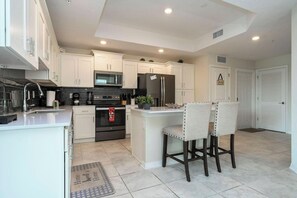A modern kitchen with white cabinets, stainless steel appliances, and a central island with two bar stools. - 3151 PC - Storey Lake Escape (Kissimmee)