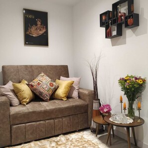 A living room with a brown sofa, patterned cushions, a vase with flowers, and a small table with candles. - Apartment with mountain view + swimming pool, gym and WiFi in Chapinero (Bogotá)