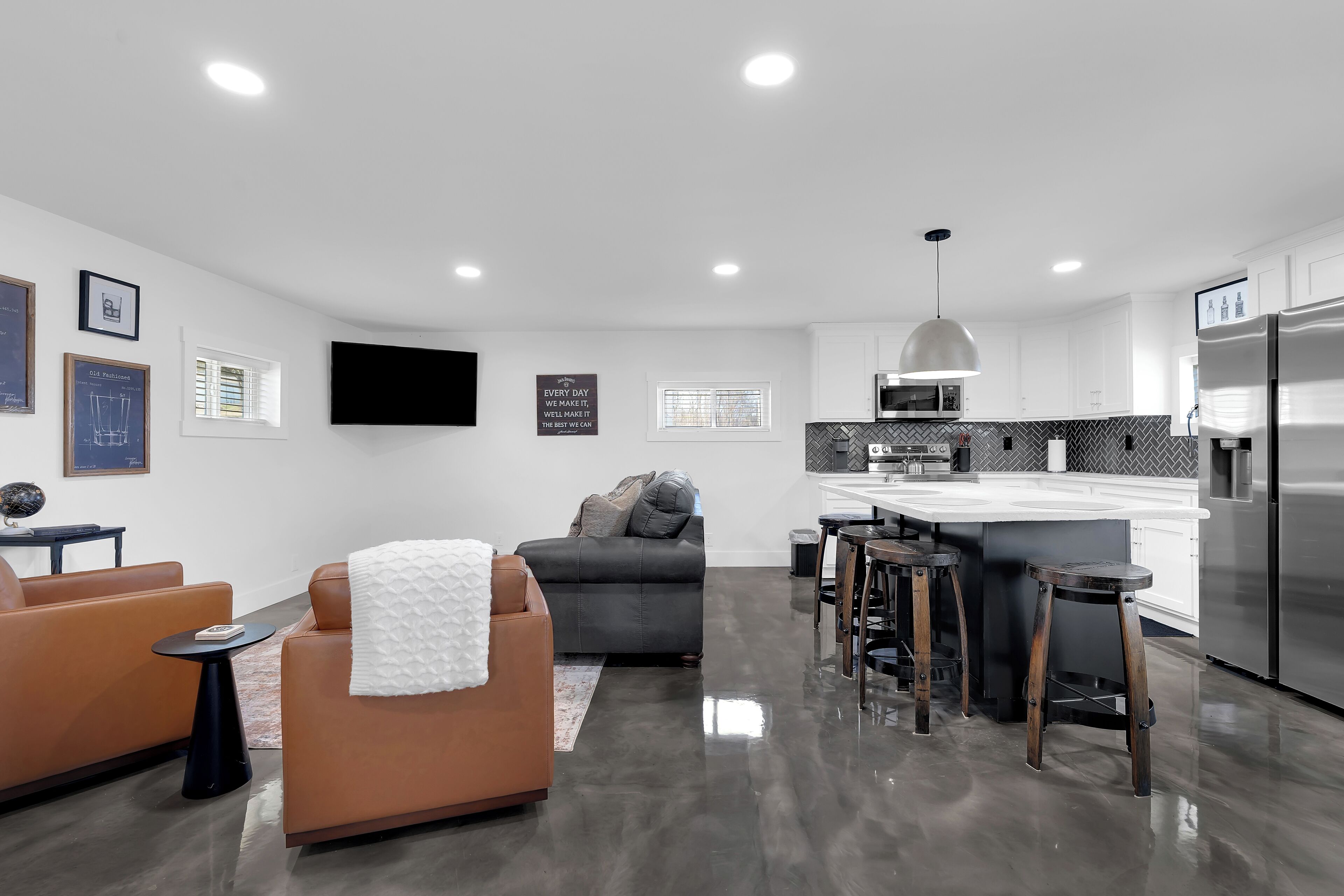 A modern kitchen with a large island, a dining area with bar stools, and a living room with a sofa and a coffee table.