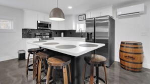 Une cuisine moderne avec des meubles blancs, un grand îlot central doté de tabourets, des appareils en acier inoxydable et un tonneau en bois.