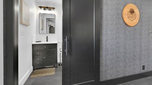 Une salle de bain moderne avec une porte sombre, un miroir et une plaque en bois accrochée au mur.
