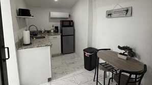A compact kitchen with white cabinets, a countertop, a sink, a microwave, and a refrigerator. There is a dining table with chairs and a small potted plant. - Cozy 1-bedroom studio in perfect Tampa with AC (Tampa)