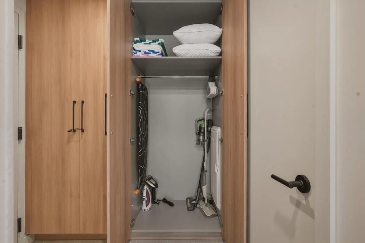 A wardrobe with a hanging rack, a shelf with folded blankets, and a vacuum cleaner.