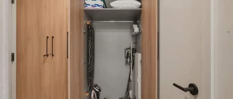 A wardrobe with a hanging rack, a shelf with folded blankets, and a vacuum cleaner.