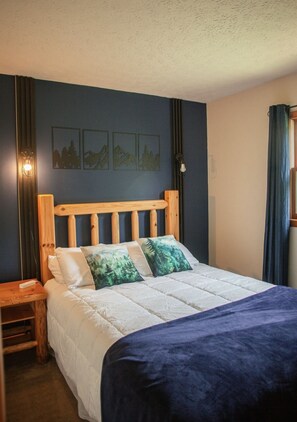 A bedroom with a wooden headboard, a bed with white bedding and green pillows, a nightstand, and wall art depicting nature scenes. - Heart of the Hocking Hills Lodge Newly renovated (Rockbridge)