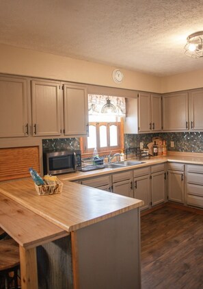 A kitchen with wooden cabinets, a microwave, a sink, and a window with a decorative lamp. - Heart of the Hocking Hills Lodge Newly renovated (Rockbridge)