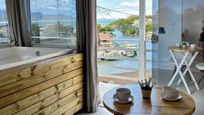 Ein modernes Zimmer mit einer hölzernen Bank, einem kleinen Tisch mit Tasse und Untertasse und Blick auf einen Jachthafen mit Booten.