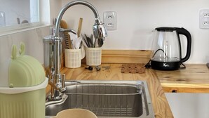 Eine Küche mit Holzarbeitsplatte, Spüle und Wasserkocher. Über der Arbeitsplatte befinden sich Regale mit Gläsern und einer Pflanze.