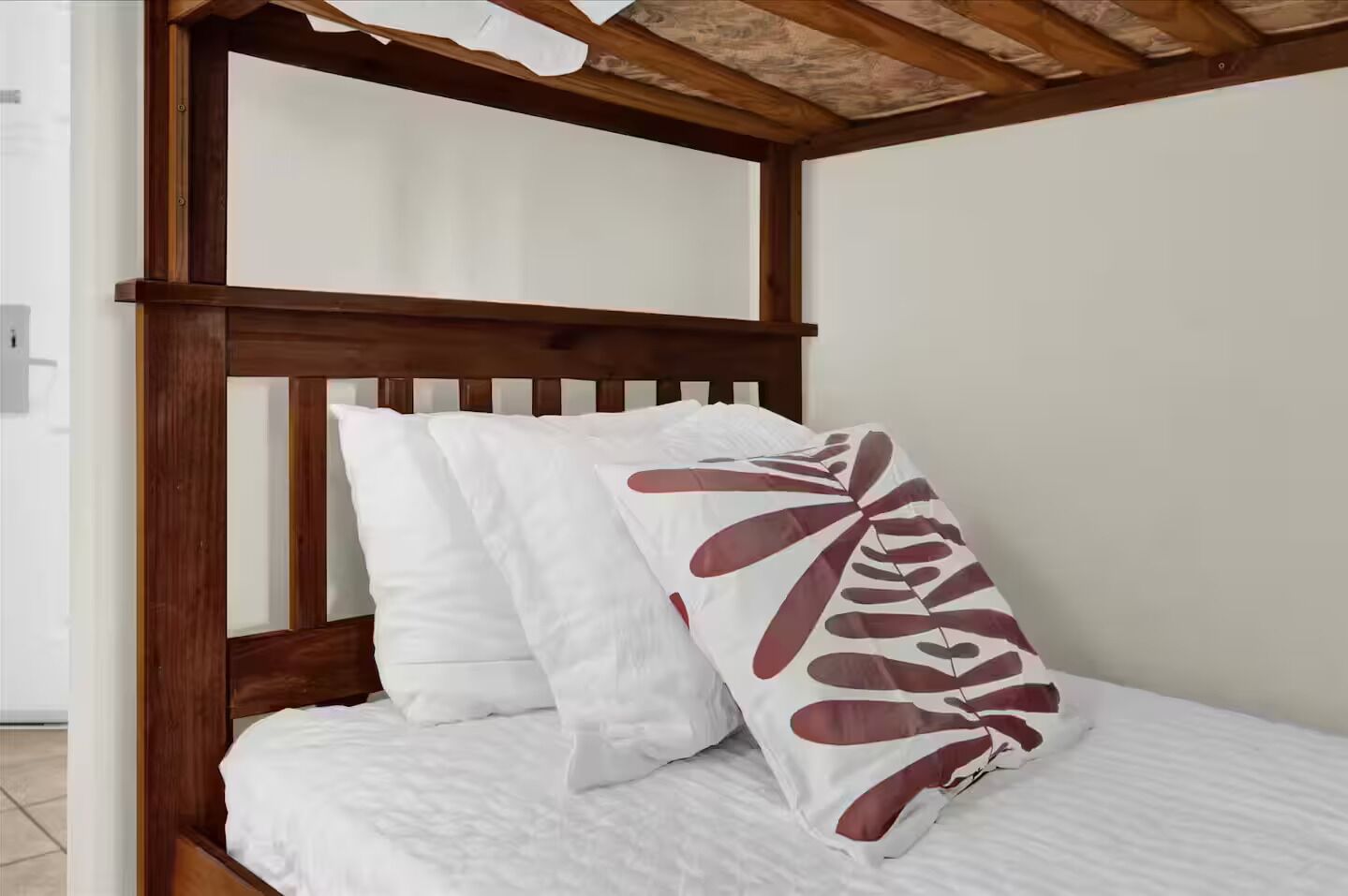 Een houten hemelbed met witte beddengoed en een enkel decoratief kussen met een bladmotief.