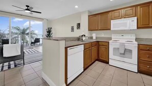 A modern kitchen with wooden cabinets, a white stove, and a dishwasher. There is a balcony with a view of palm trees. - Trendy Lake Condo-Disney view! (Orlando)
