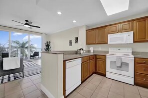 A modern kitchen with wooden cabinets, a white stove, and a dishwasher. There is a balcony with a view of palm trees. - Trendy Lake Condo-Disney view! (Orlando)